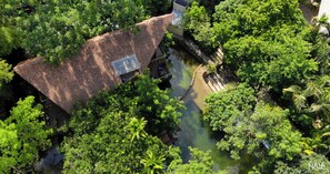 Ein Haus mit Schrägdach, umgeben von üppiger Vegetation und einem kleinen Wasserspiel.