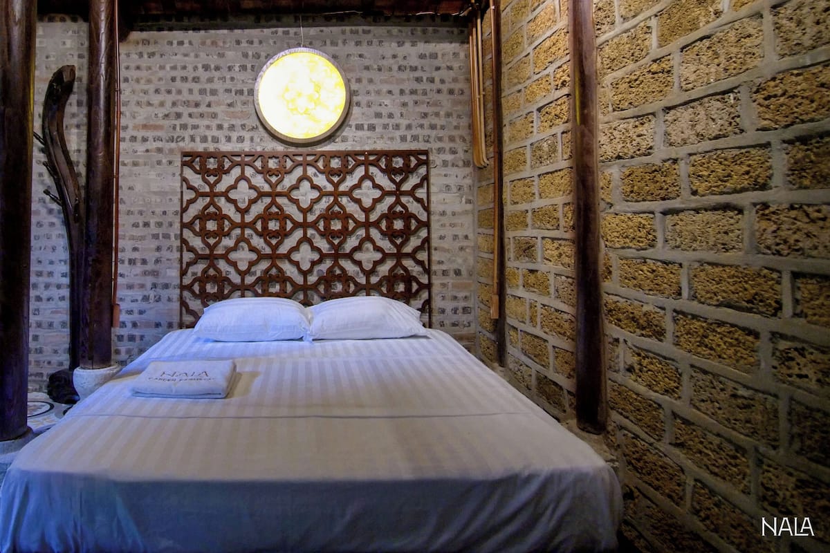 Un lit bien fait, avec une tête de lit à motifs, un applique murale ronde et un sol carrelé.