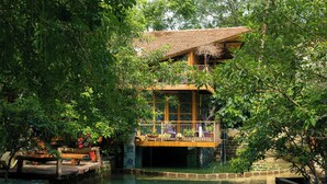 Een traditioneel houten huis met een balkon dat uitkijkt op een vijver, omringd door weelderige begroeiing.