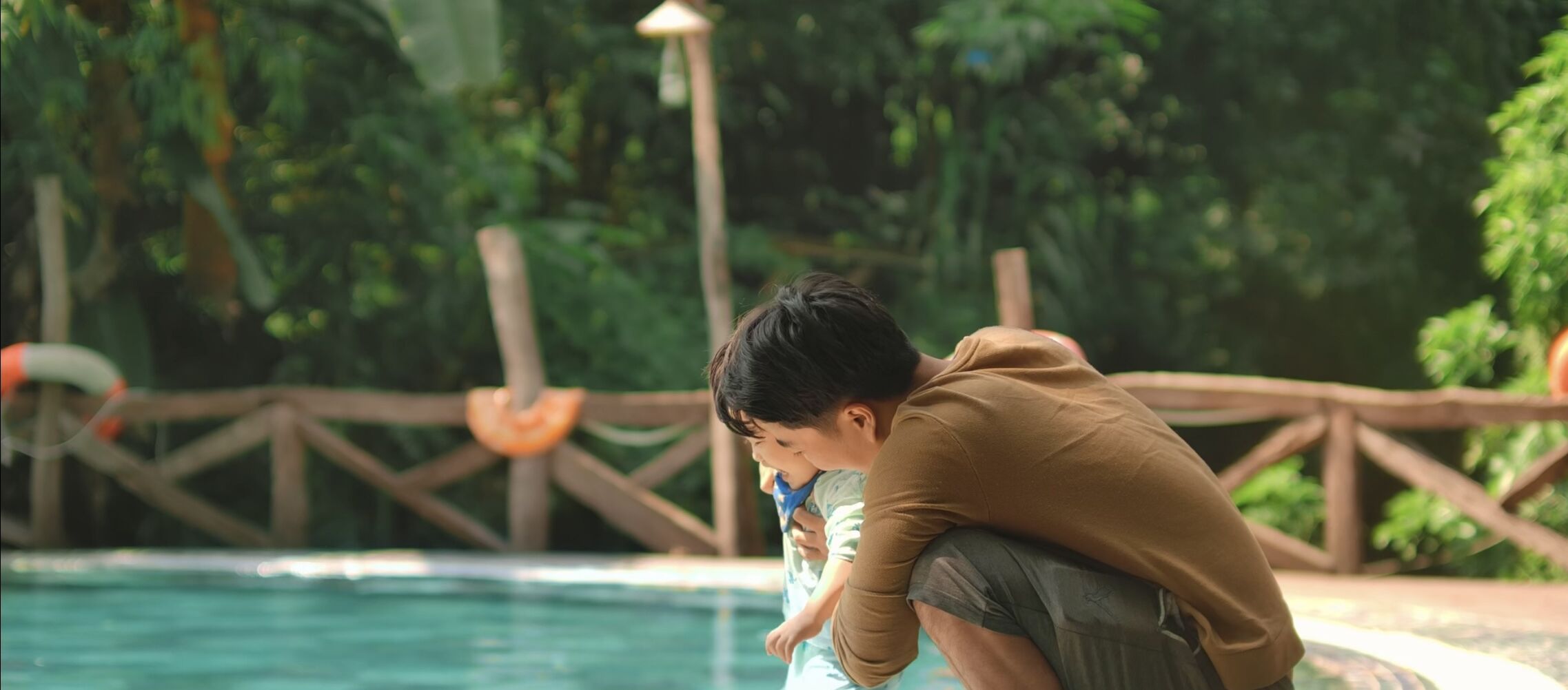 A pool area with a wooden fence and greenery in the background.