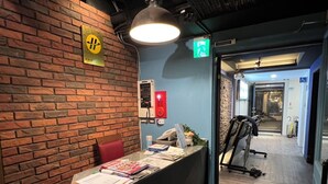 A reception desk with a brick wall, a sign with a symbol, and a treadmill in the background.