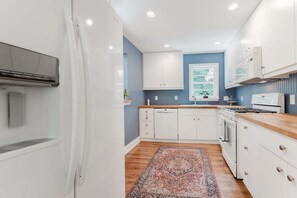 A modern kitchen with white cabinets, a wooden countertop, and a patterned rug.