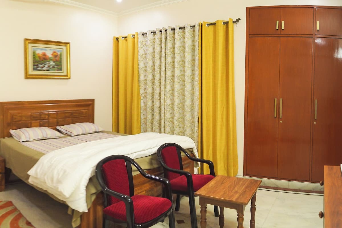 A bedroom with a bed, two chairs, a small table, a wardrobe, and a painting on the wall.