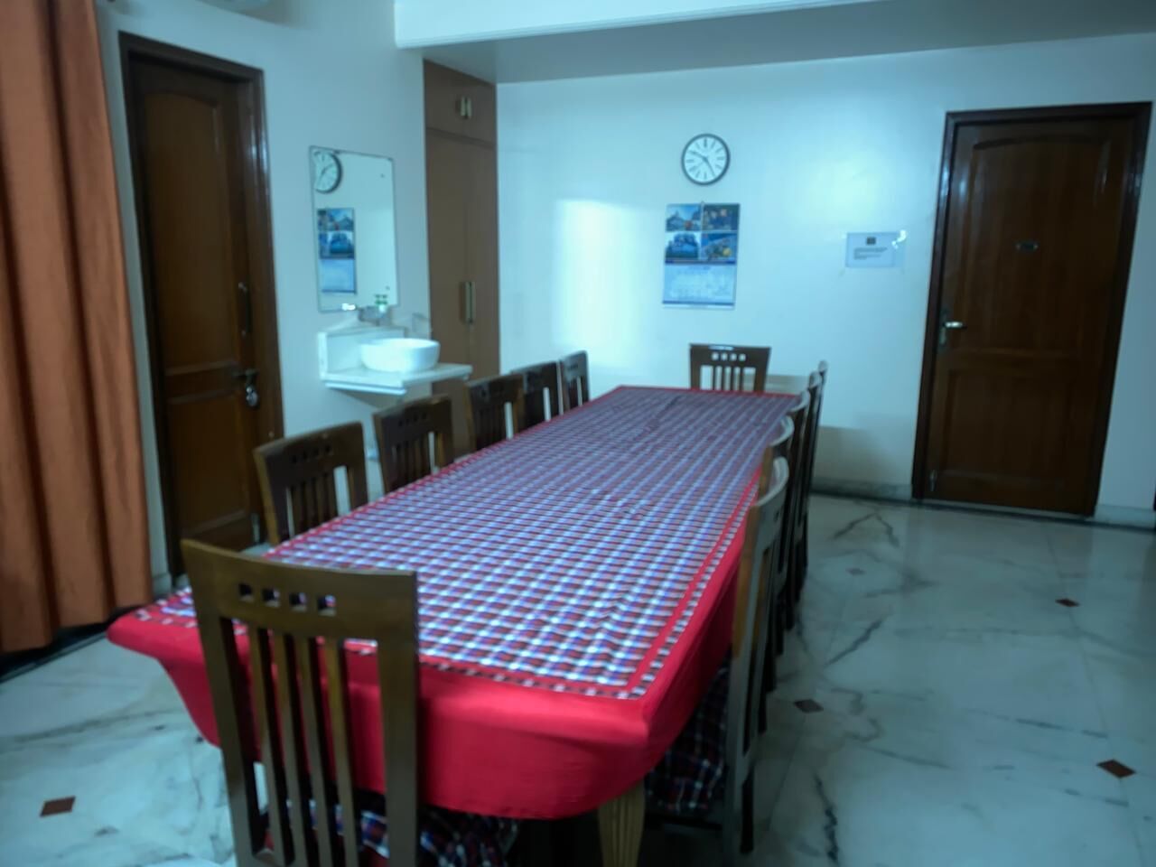A dining area with a rectangular table covered by a red tablecloth, surrounded by wooden chairs.
