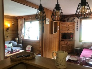 Interior acollidor d'una cabana amb parets de fusta, zona de dinar amb taula per a dues persones, zona de cuina i finestra amb vista a un cervell fora.
