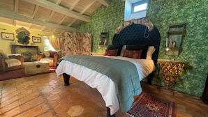 Un dormitorio con una cama grande, un cabecero de madera, una pared verde, una ventana pequeña y un suelo de piedra.