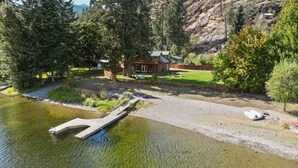 A lodge with a dock extending into a lake, surrounded by trees and a hilly backdrop. - Casa Twin Lakes | Private Dock, Lake View, Fire Pit, Large Yard, Near Silverwood (Rathdrum)