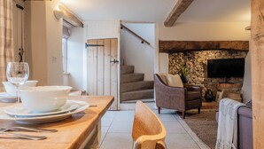 Un coin repas avec une table en bois dressée pour deux personnes, un canapé et une cheminée en pierre.