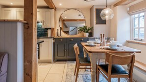 Une cuisine avec des poutres en bois, une table à manger avec des chaises, un grand miroir et une fenêtre laissant entrer la lumière naturelle.