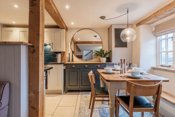 A kitchen with wooden beams, a dining table with chairs, a large mirror, and a window with natural light. - The Gamekeeper's Cottage-Stunning 2 Bed (Witney)