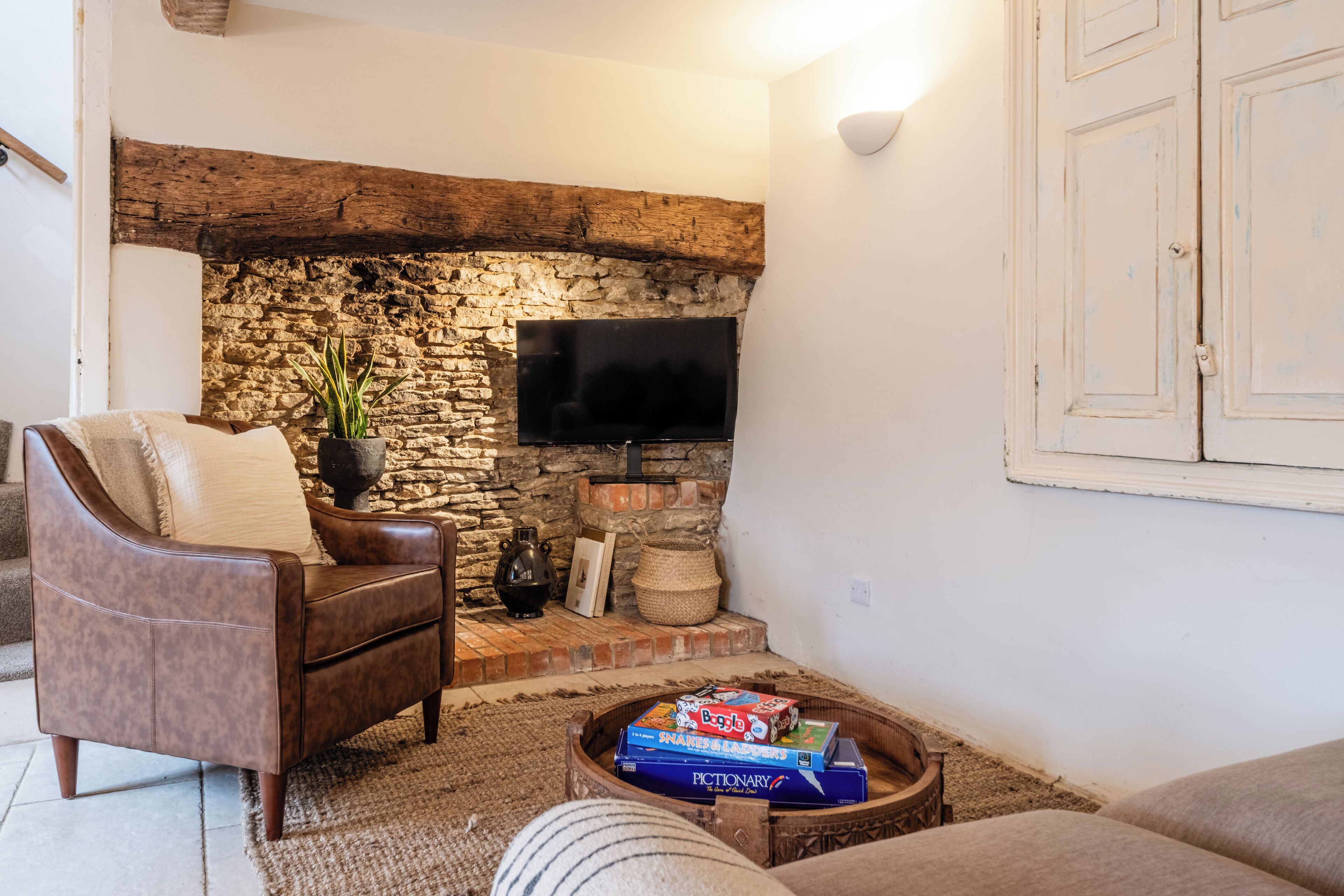 A cozy living room with a stone fireplace, a leather armchair, a television, and a coffee table with books.