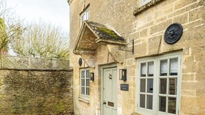 Un bâtiment en pierre avec une porte verte, une enseigne indiquant « Gamelan's Cottage », et une fenêtre à carreaux multiples.
