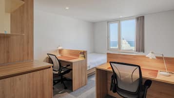 Habitación de hotel con un escritorio de madera, dos sillas, una cama y una ventana con cortinas.