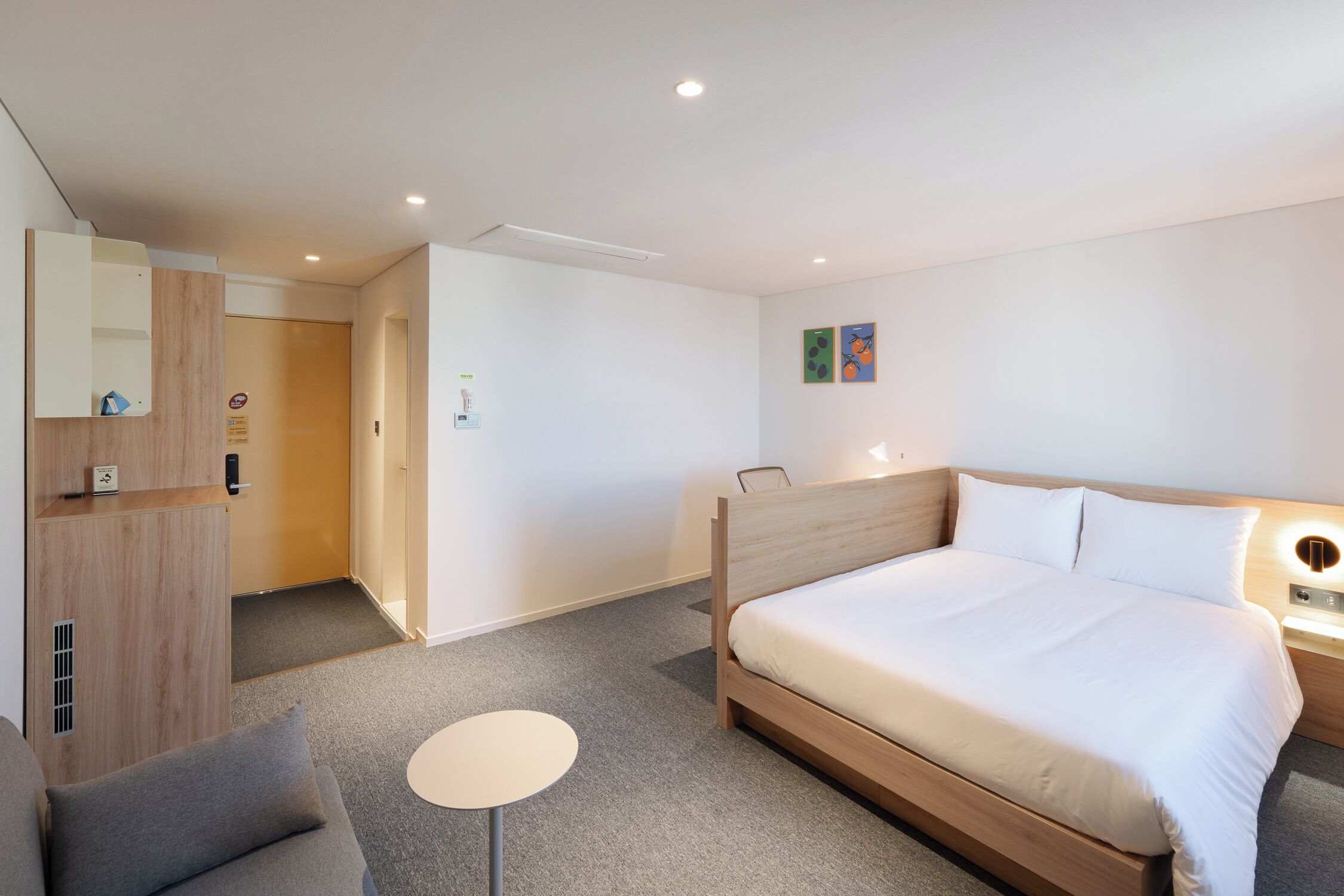 A hotel room with a wooden bed, a small round table, a sofa, a mirror, and a door leading to another room.