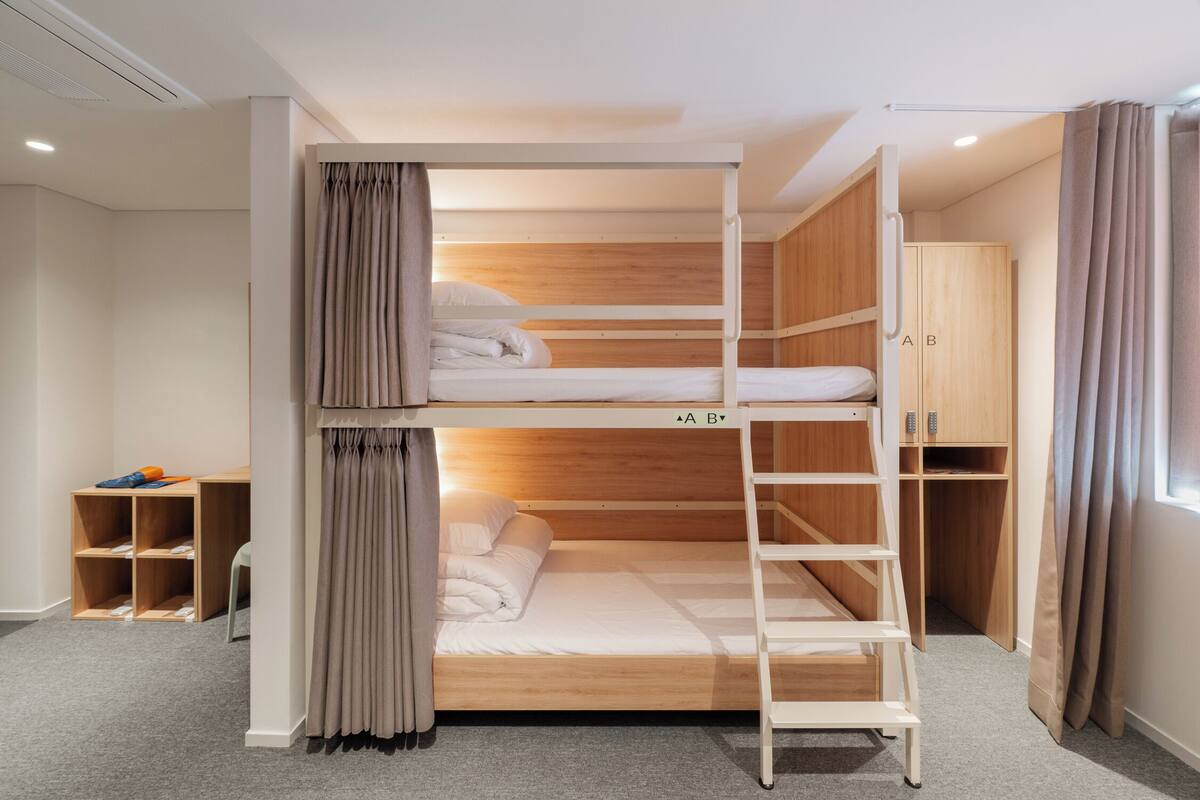 A bunk bed with a ladder, wooden wardrobe, and a desk with storage shelves.
