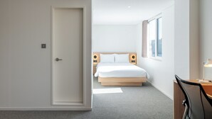 A modern hotel room with a large bed, a desk with a chair, and a view of the city through the window. - Mangrove Jeju City (Jeju City)