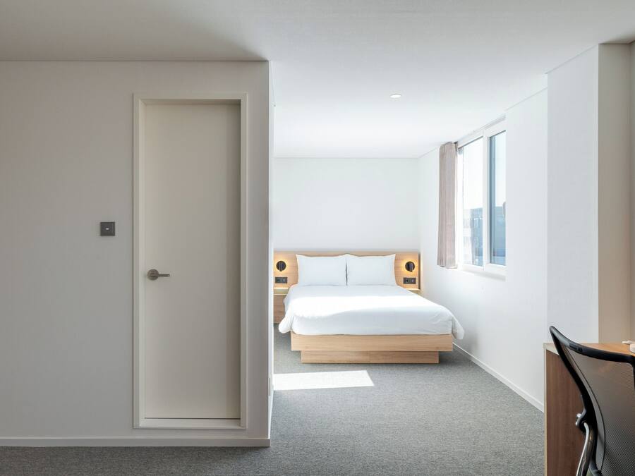 Een moderne hotelkamer met een groot bed, een bureau met stoel en uitzicht op de stad door het raam.