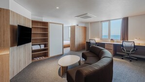 A modern hotel room with a flat-screen TV, a sofa, a desk, and a large window offering a view of the sea. - Mangrove Jeju City (Jeju City)