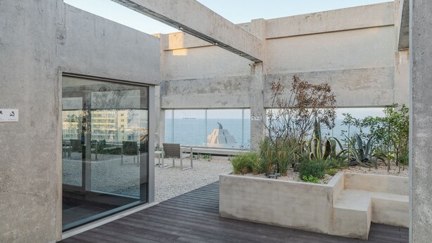 A modern outdoor terrace with a view of the sea, featuring concrete structures, a wooden deck, and a seating area. - Mangrove Jeju City (Jeju City)