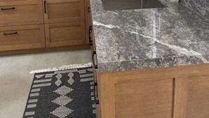 A modern kitchen with a granite countertop, wooden cabinets, a stainless steel range hood, a built-in sink, and a window with blinds.