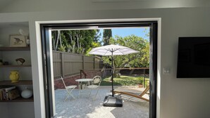 A view through a sliding glass door into an outdoor patio area with a table, chairs, and an umbrella.
