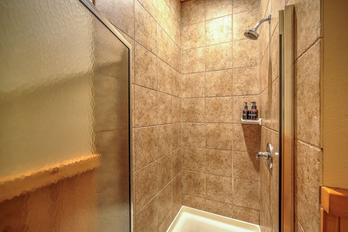 Zona de ducha con puerta de cristal, paredes con azulejos y un estante con artículos de aseo.