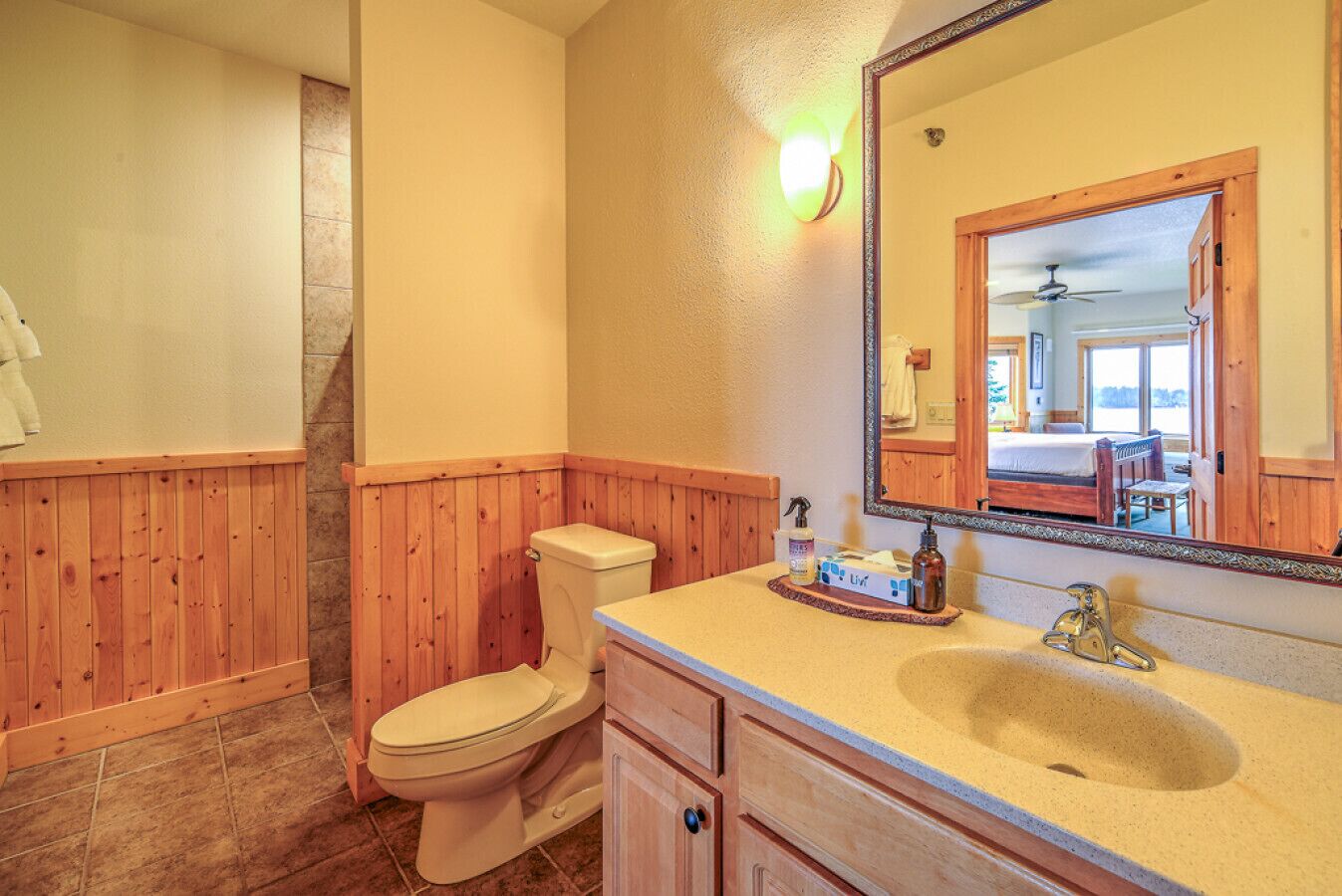 A bathroom with wooden paneling, a toilet, a sink with a mirror, and a shower area.