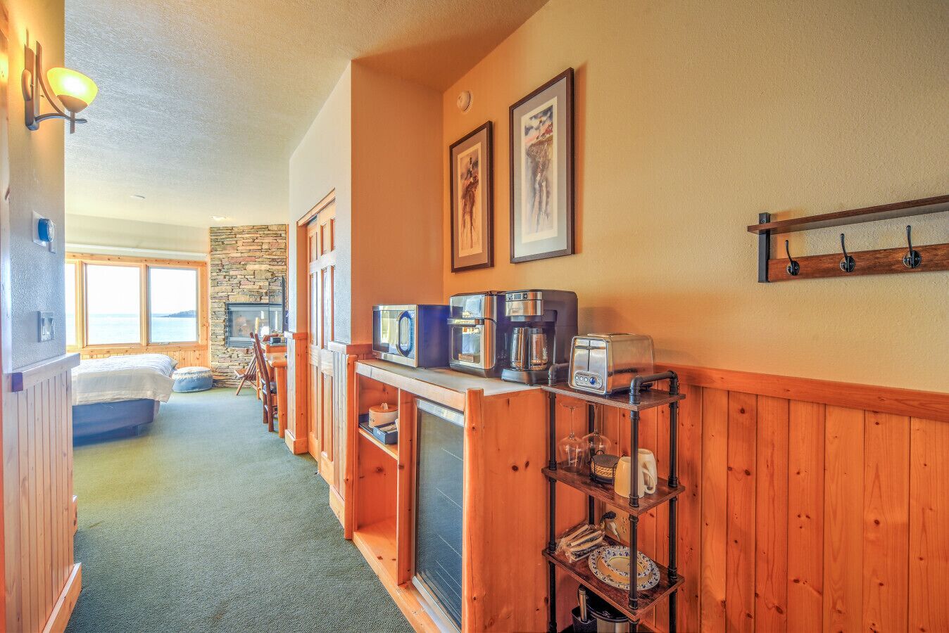 A hotel room with a bed, a stone wall, a wooden bench, a coffee station, and a view of the sea.