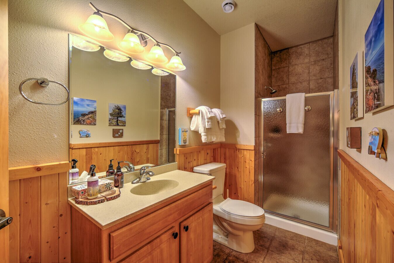 A bathroom with wooden cabinets, a sink, a toilet, and a glass-enclosed shower.