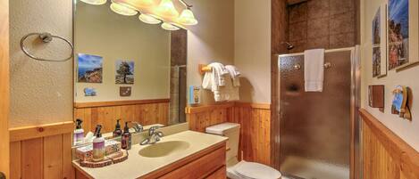 A bathroom with wooden cabinets, a sink, a toilet, and a glass-enclosed shower.