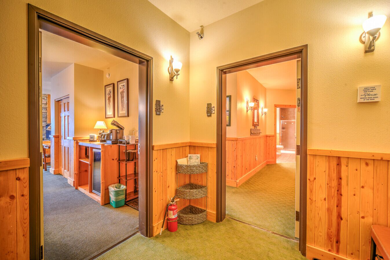 A hallway with wooden walls and doors leading to a room with a desk, lamp, and framed pictures.