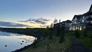 Blick auf einen See mit einem Weg, der zu einer Reihe mehrstöckiger Gebäude führt, vermutlich ein Hotel oder Resort.