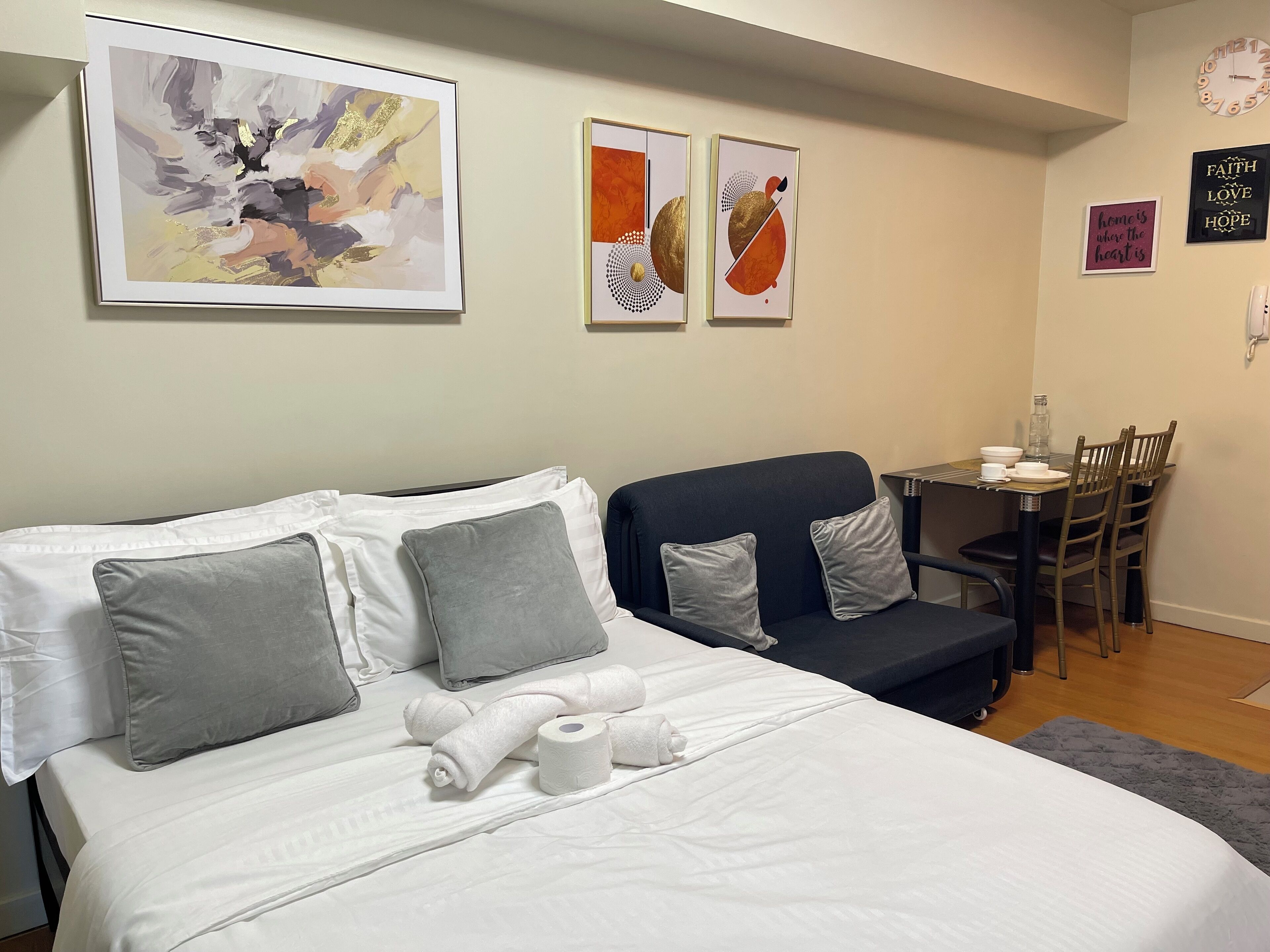 Una habitación de hotel con cama, un sofá, una mesita con una silla y obras de arte en las paredes.
