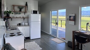 A modern kitchen with white appliances, a dining area with a view, and a wooden deck. - Pinnacolo Farm Stay (Pinnacle)