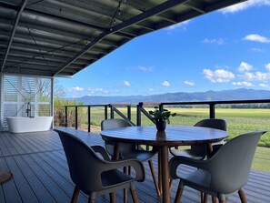 A covered outdoor seating area with a table and chairs, overlooking a scenic landscape with mountains and fields.