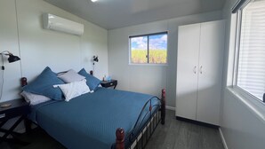 A bedroom with a bed, bedside tables, a wardrobe, an air conditioning unit, a window, and a lamp. - Pinnacolo Farm Stay (Pinnacle)