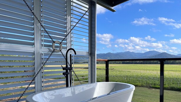 A white freestanding bathtub on a wooden deck with a view of a green field and mountains in the background. - Pinnacolo Farm Stay (Pinnacle)