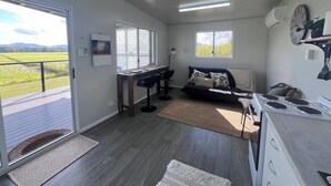 A modern kitchen with a stove, a dining area with a table and chairs, a sofa, and a large window offering a view of a green landscape. - Pinnacolo Farm Stay (Pinnacle)