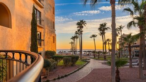 A pathway leading to a building with a balcony, surrounded by palm trees and a clear sky.