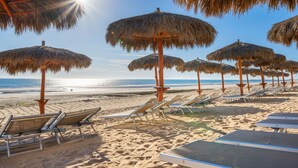 A beach with thatched umbrellas and sun loungers.