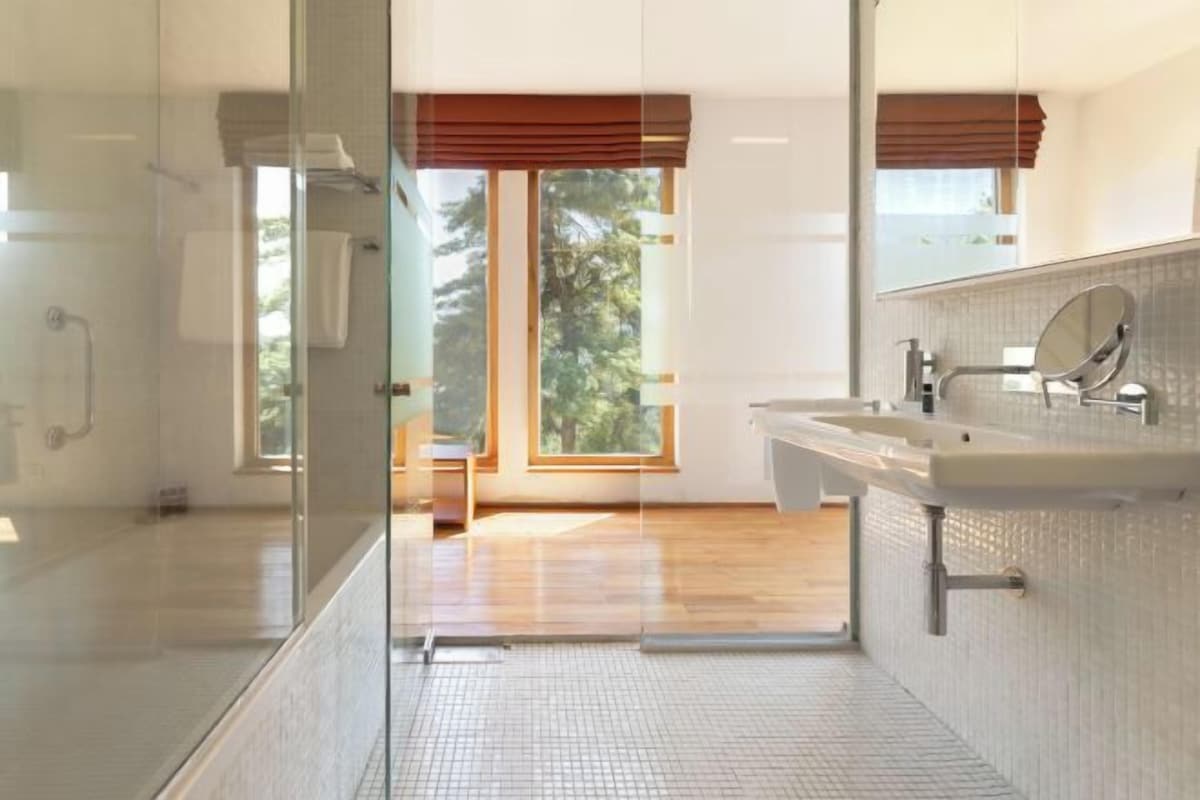 A modern bathroom with a glass shower enclosure, a large window, and a vanity with a mirror.