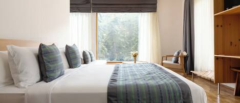 A neatly made bed with a striped blanket, a bedside table with a vase, and a view of trees through the window.