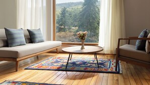 A living room with a sofa, a round coffee table, and a view of a forest through large windows. - Zhiwaling Ascent (Thimphu)