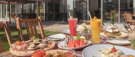 An outdoor dining area with various dishes, drinks, and a view of the building in the background.
