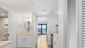 Une salle de bain moderne avec un grand miroir, des meubles blancs et une vue sur l’extérieur.