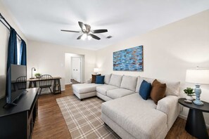 Un salon moderne avec un canapé d’angle, une table à manger et un ventilateur de plafond.