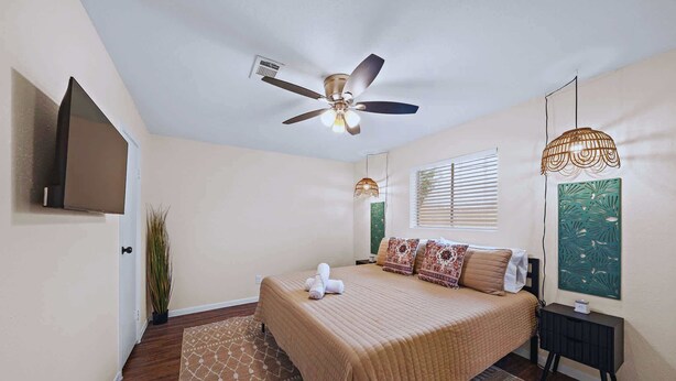 A bedroom with a bed, a ceiling fan, a TV, a window with blinds, a wall-mounted artwork, and a bedside table. - Cozy Coastal Stay: Near Kemah + NASA | BBQ | Beach (Seabrook)