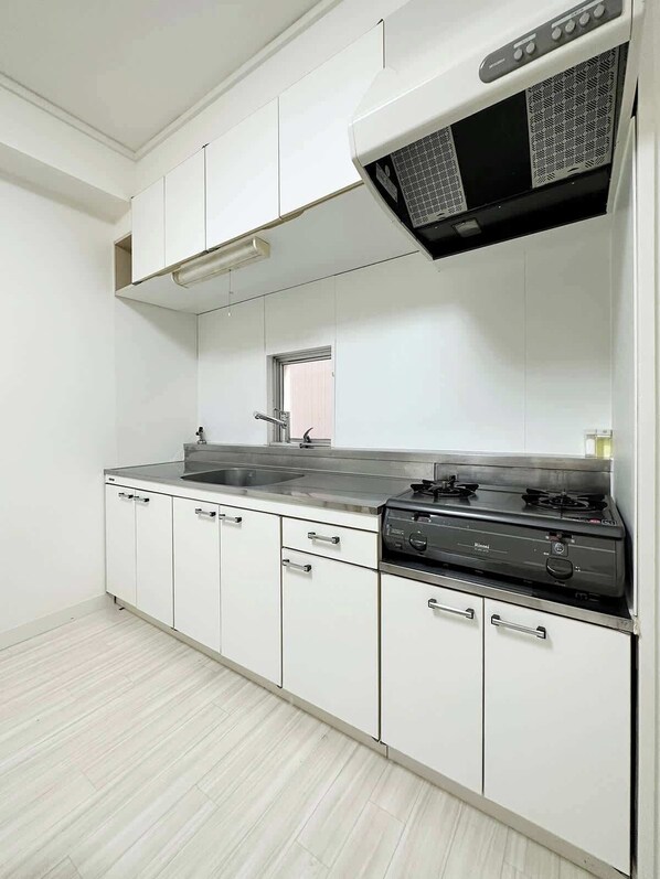 Una cocina moderna con armarios blancos, encimera de acero inoxidable, estufa a gas y campana extractora.