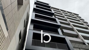 Een modern gebouw met een opvallend ‘b’ logo op de gevel, met een geometrisch ontwerp, balkons en een plat dak.
