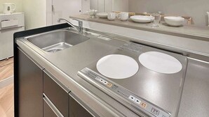 Eine moderne Küche mit einer Edelstahl-Spüle, zwei weißen Induktionskochfeldern und einer schwarzen Dunstabzugshaube.